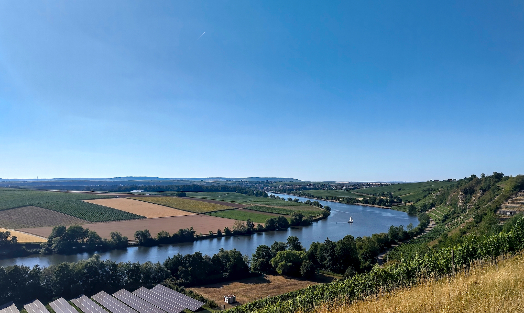 Blick über den Neckar: Eine Panoramaaussicht auf den Neckar bei Lauffen. Die Gegend ist geprägt von historischen Weinbergen mit Natursteinmauern. Die Region bietet Wanderwege wie den Panoramaweg bei Neckarwestheim. Der Krappenfelsen – am rechten Bildrand zu sehen – ist ein beliebter Aussichtspunkt.