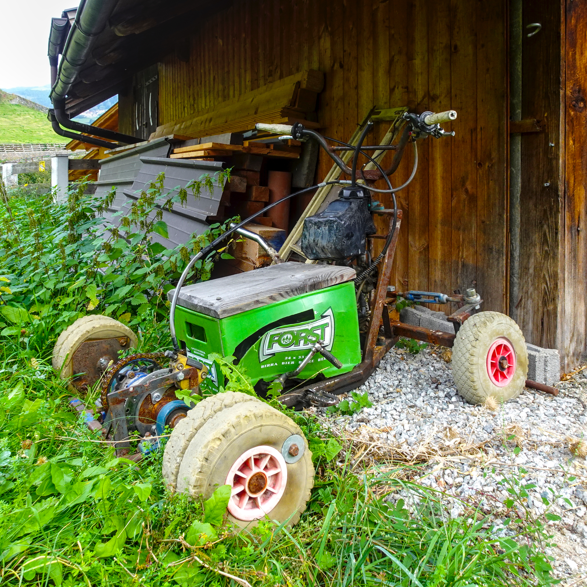 Das Bild zeigt eine selbstgebaute fahrende Bierkiste (Motorisierte Bierkiste), die mit einer grünen Kiste der Marke Forst (Südtiroler Bier) und einem kleinen Motor ausgestattet ist.