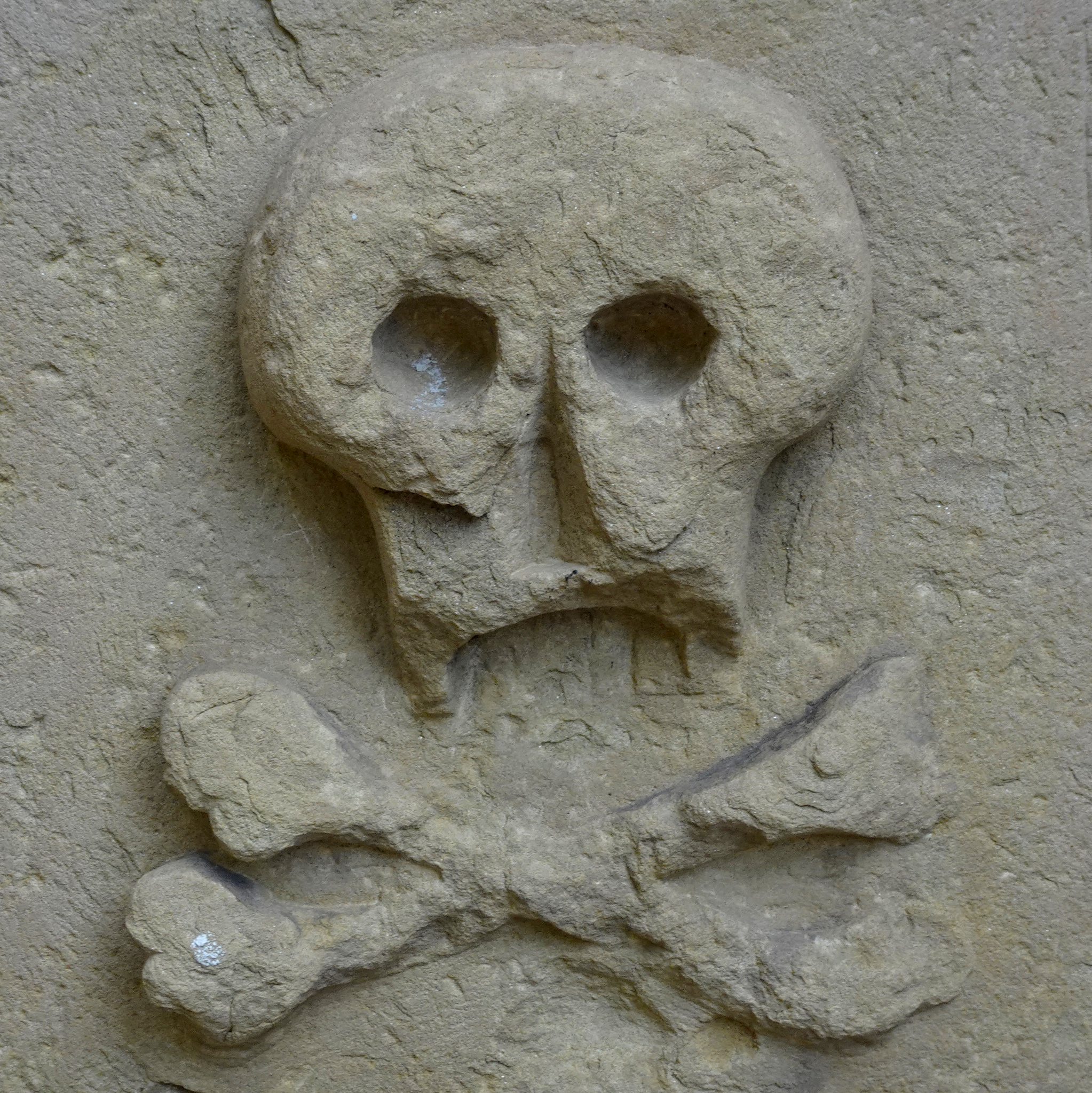 Radtour zum Kloster Maulbronn – Hier in Maulbronn – Dieses Bild zeigt ein eingemeißeltes Relief eines Totenkopfs mit gekreuzten Knochen auf einem historischen Grabstein aus Sandstein.